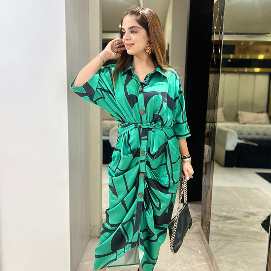 Woman wearing an emerald green draped shirt dress with abstract leaf print, button-down front, waist tie, and black heels – stylish women's midi dress for brunch or resort wear.