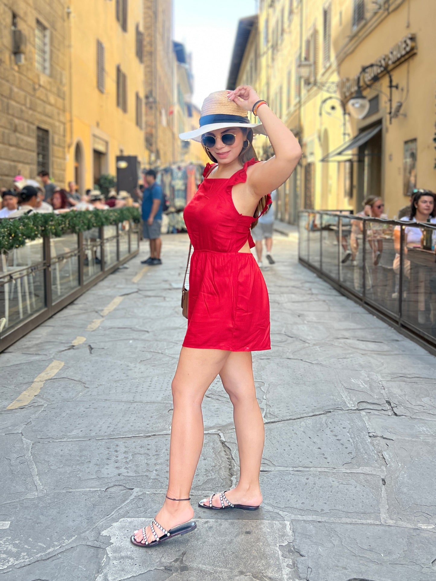 Woman wearing a bold red tie-shoulder romper with sunhat and heels in a European street