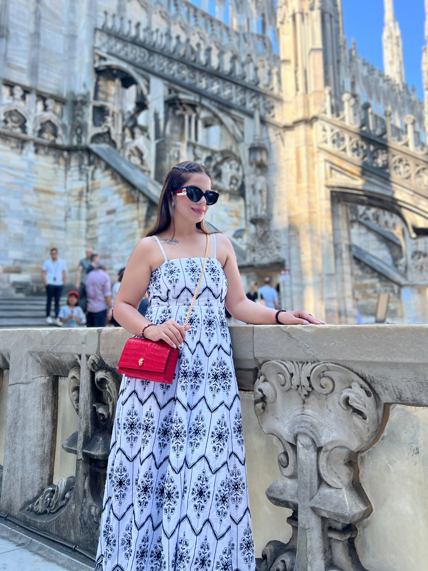 Woman in a white maxi dress with black tile print and spaghetti straps, standing in front of gothic architecture