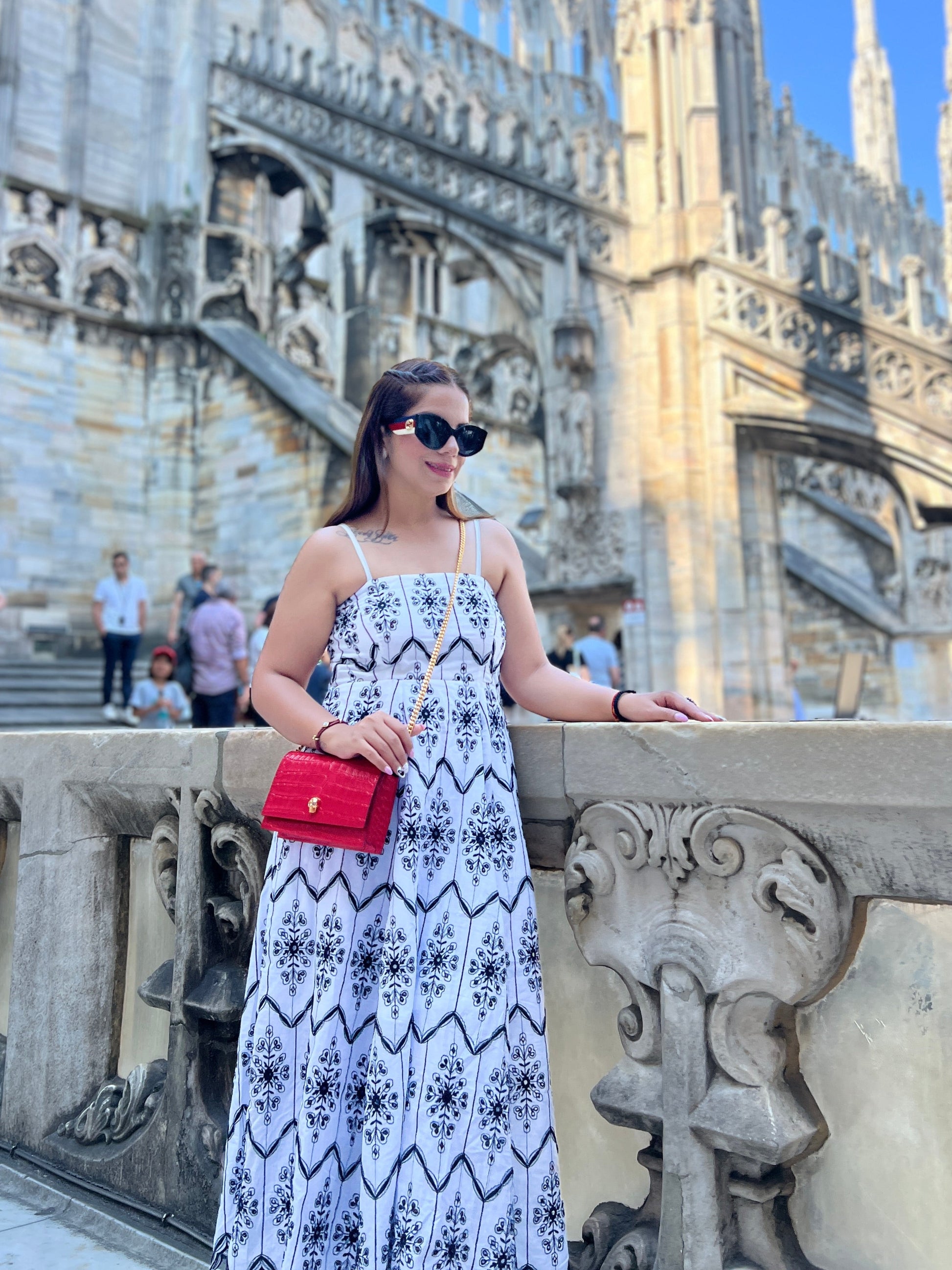 Woman in a white maxi dress with black tile print and spaghetti straps, standing in front of gothic architecture